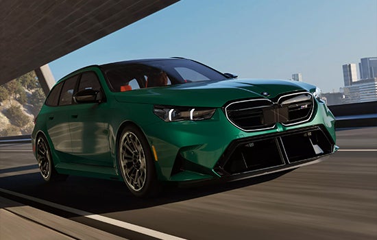 Green BMW M5 Touring driving on a city road. | BMW of Dayton in Dayton OH